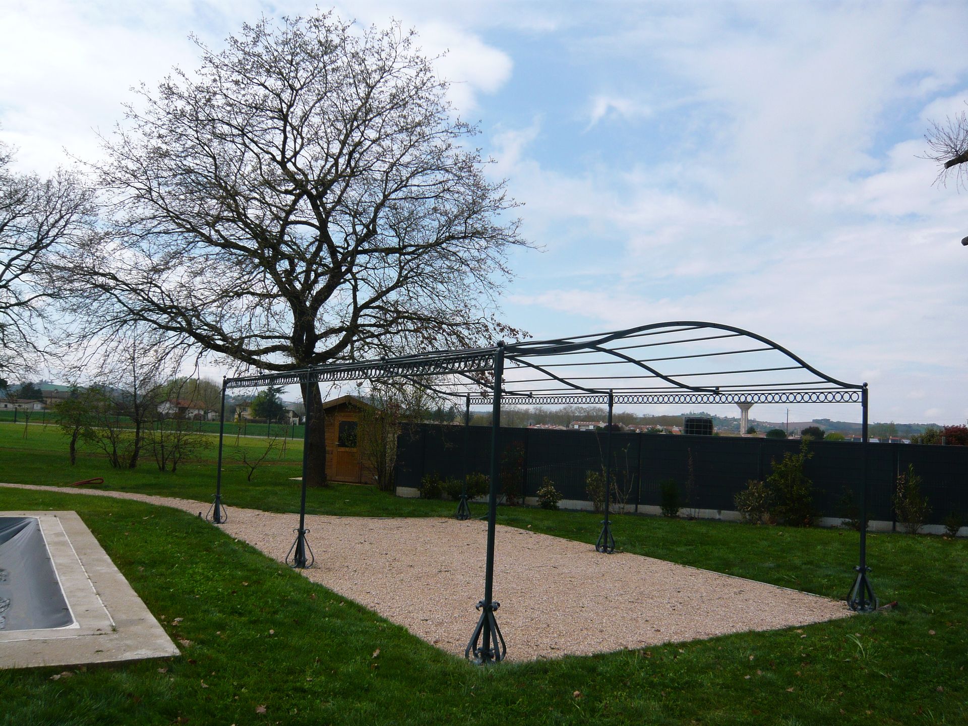 Terrasse en gravier avec un auvent métallique, jouxtant une pelouse.
