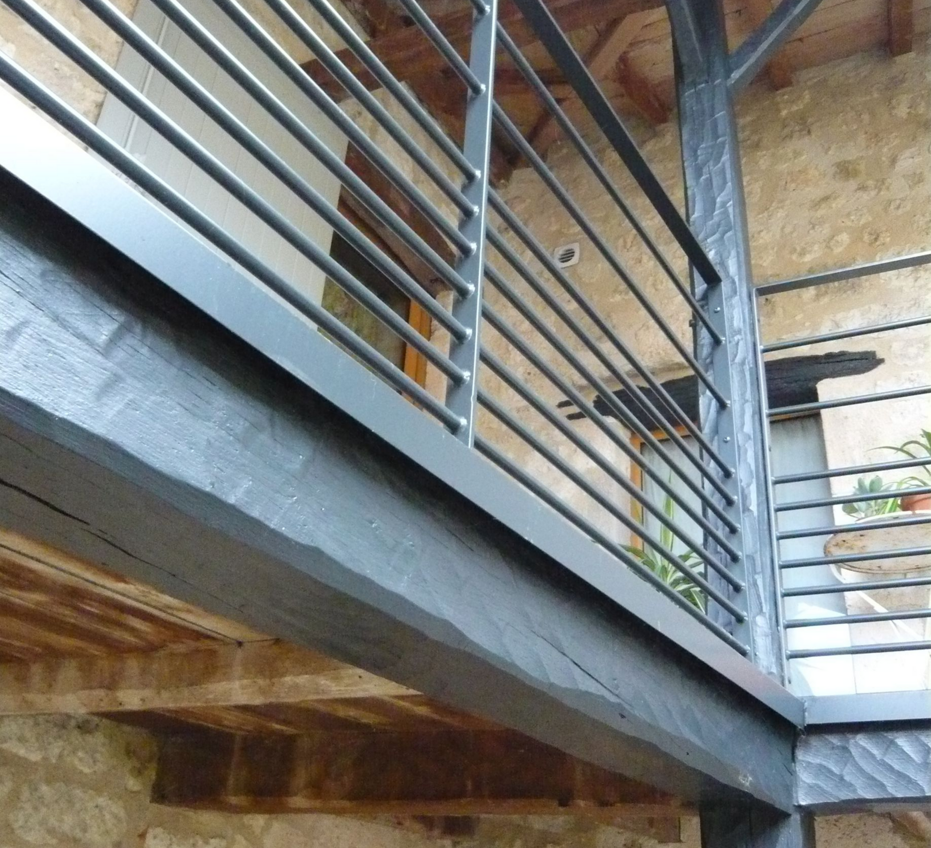 Rambarde métallique à barreaux horizontaux sur un balcon en bois donnant sur un bâtiment.
