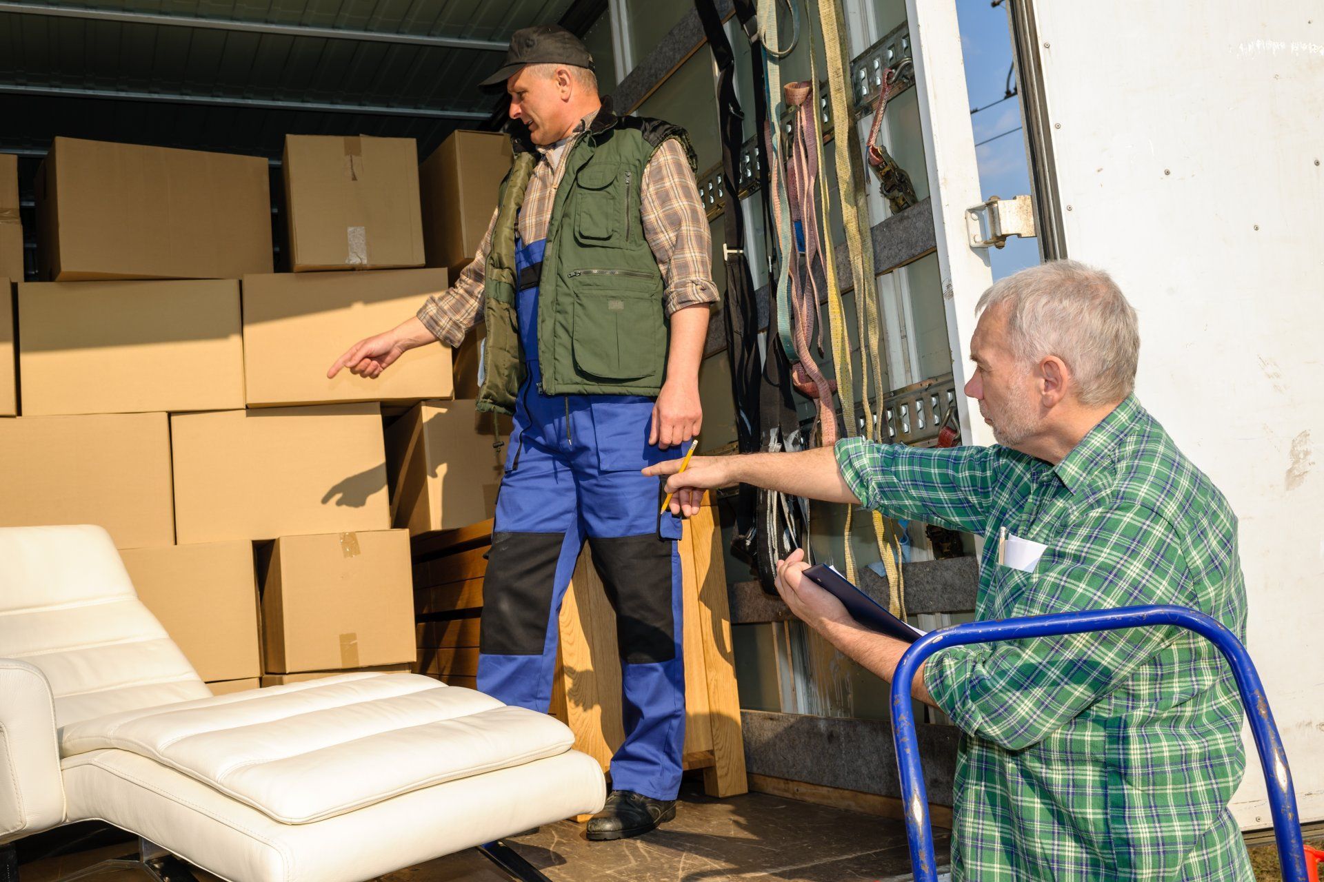 Deux hommes déchargent des cartons d'un camion, l'un debout à l'intérieur et l'autre assis à l'extérieur avec un diable.