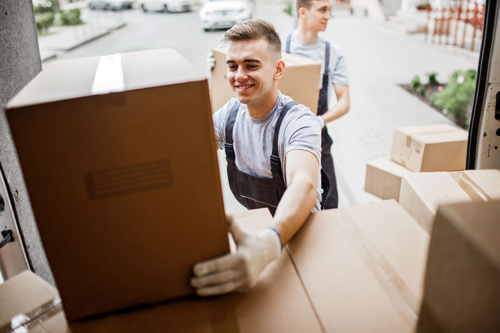 Deux déménageurs transportent des cartons dans une maison, l'un d'eux sourit au premier plan.