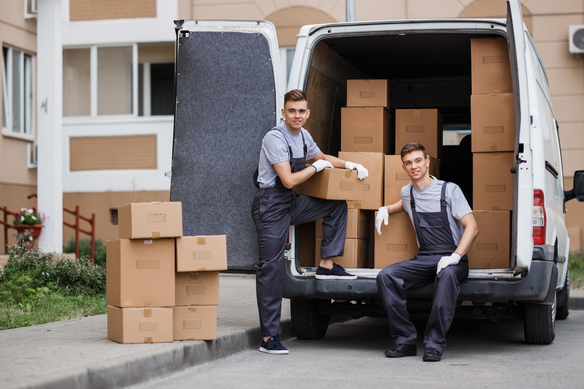 Deux déménageurs chargent des cartons dans une camionnette de livraison devant un immeuble.