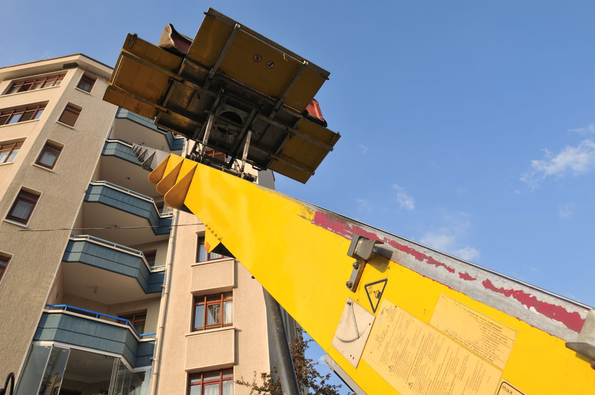 Une grue de chantier soulève une grande plateforme à côté d'un immeuble d'habitation sous un ciel bleu.