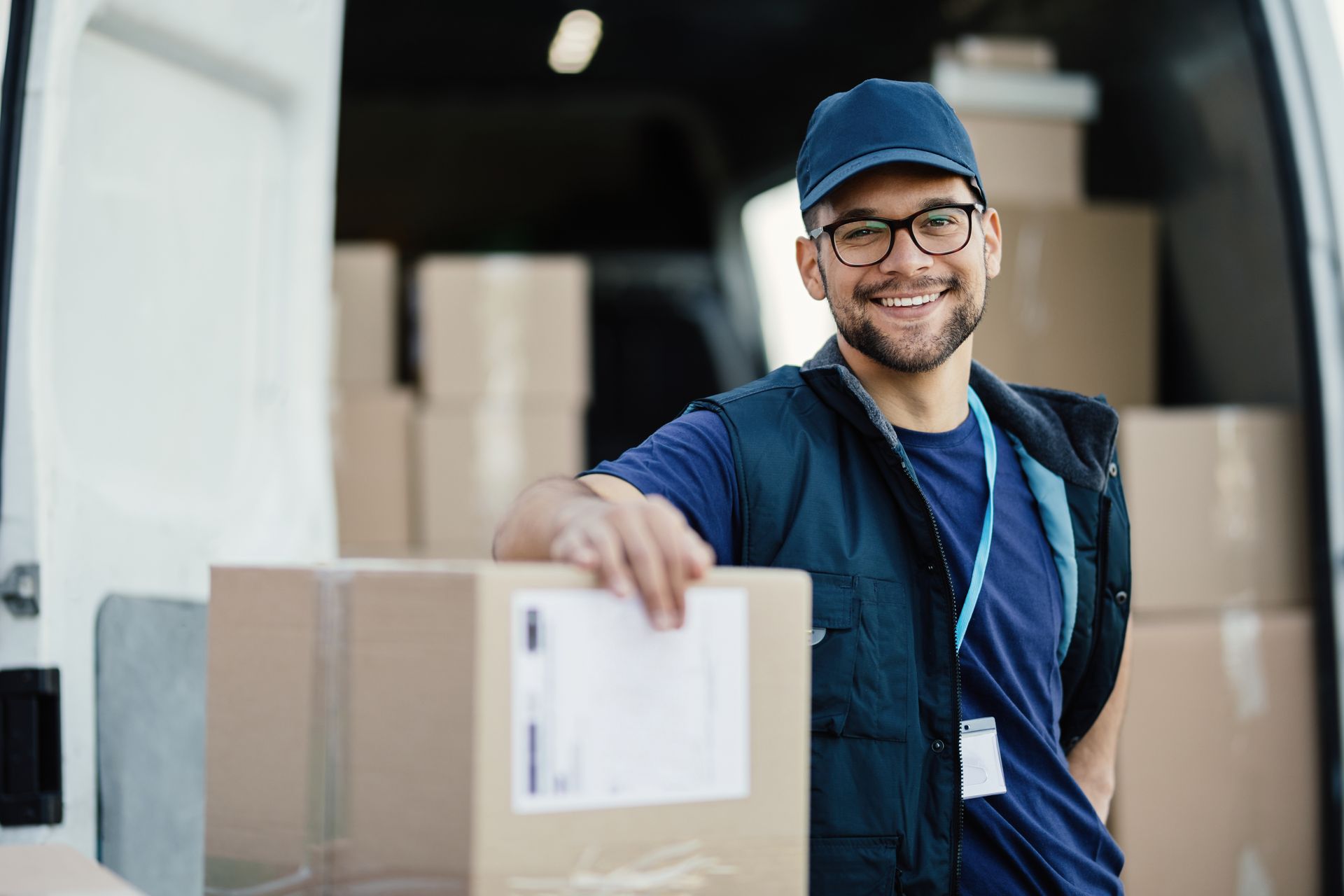Livreur souriant à côté de cartons empilés dans la zone de chargement d'une camionnette ouverte