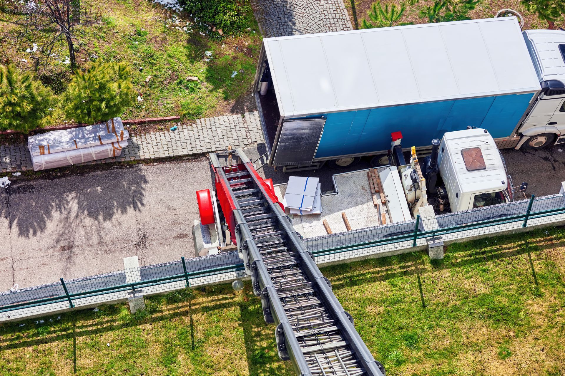 Vue aérienne d'un téléphérique rouge à côté d'un camion blanc et d'un bâtiment bleu sur un site industriel herbeux