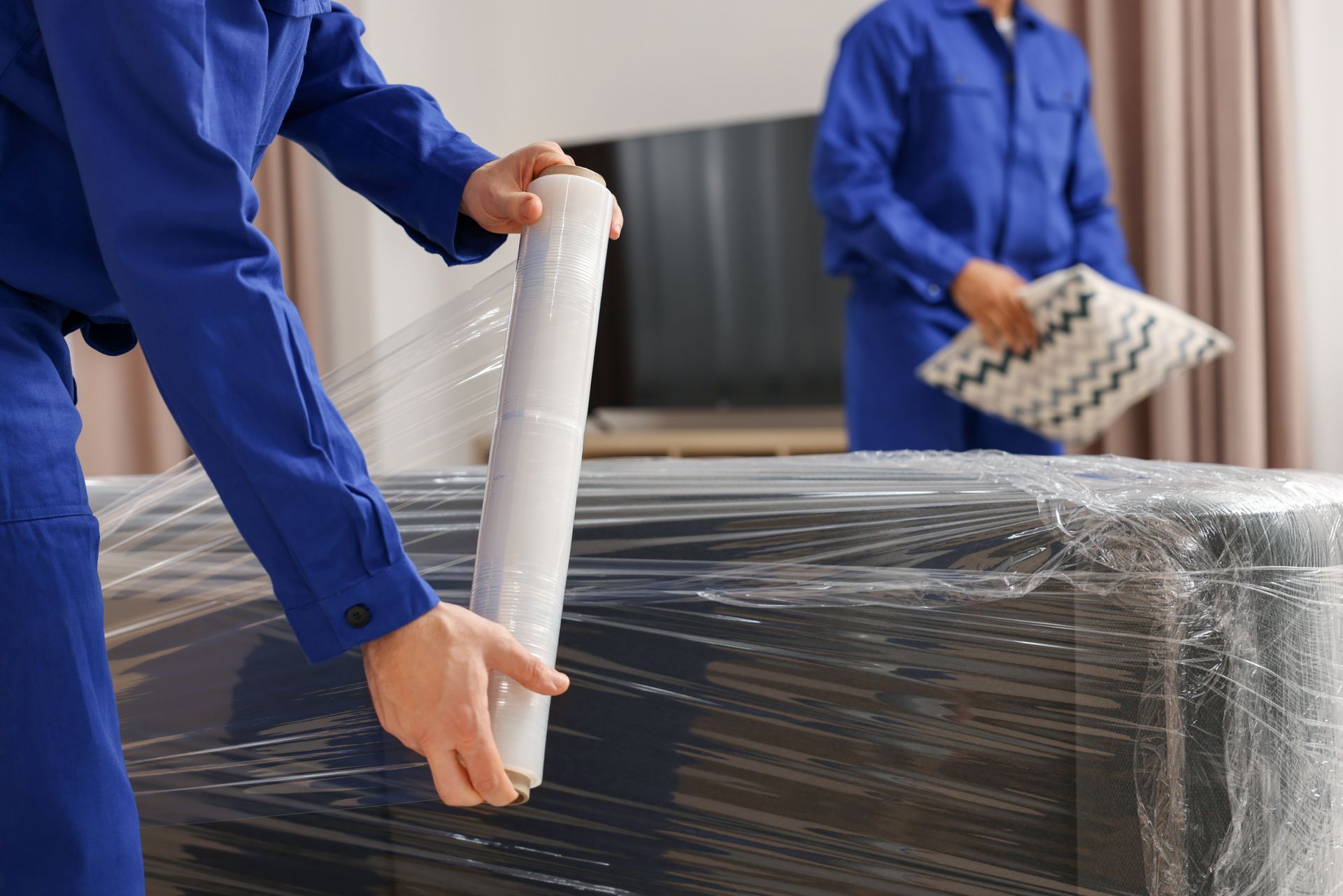 Des ouvriers en uniforme bleu emballent un gros objet dans du film plastique transparent.