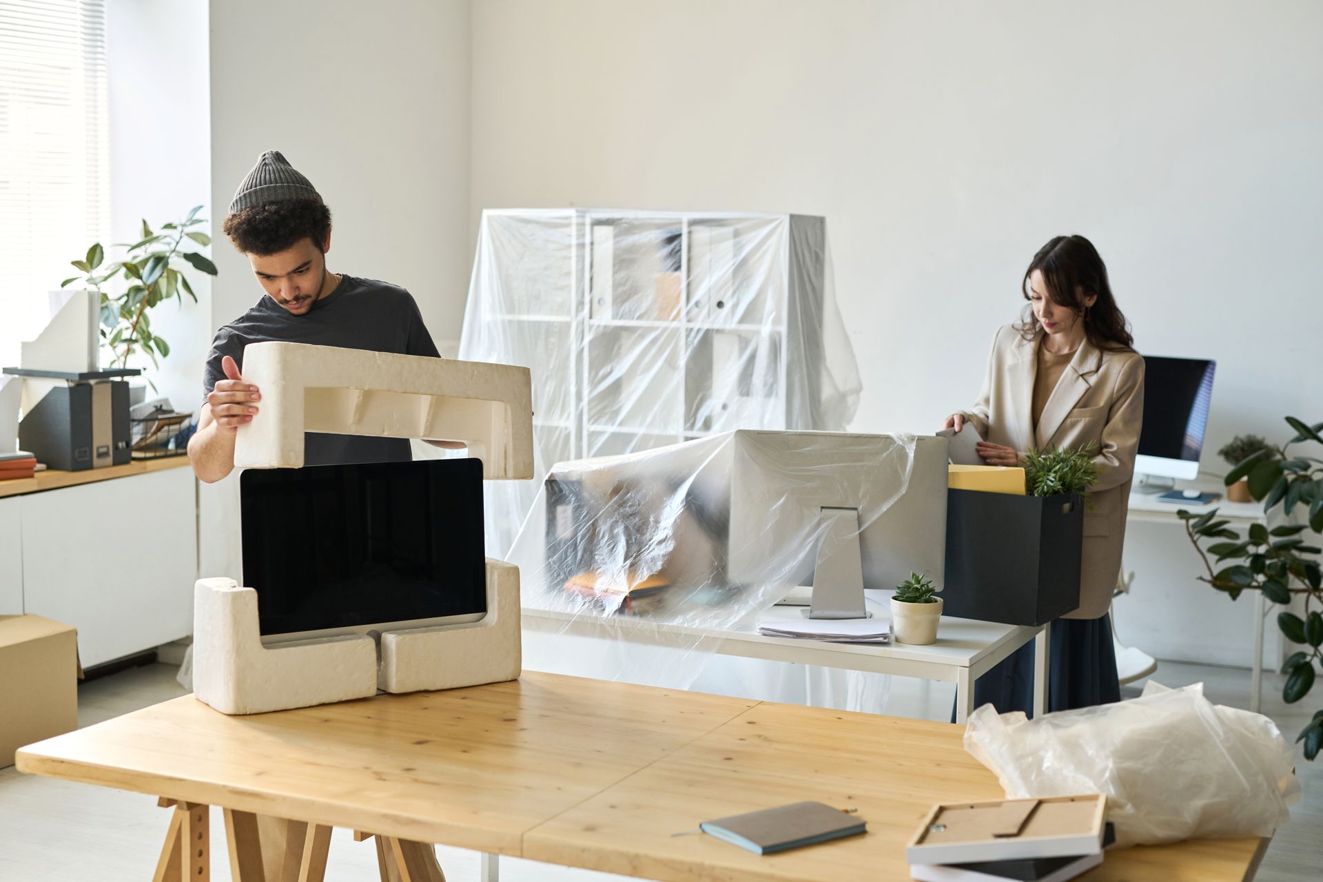Des personnes emballent et déballent des cartons dans un bureau lumineux dont le mobilier est recouvert de plastique.