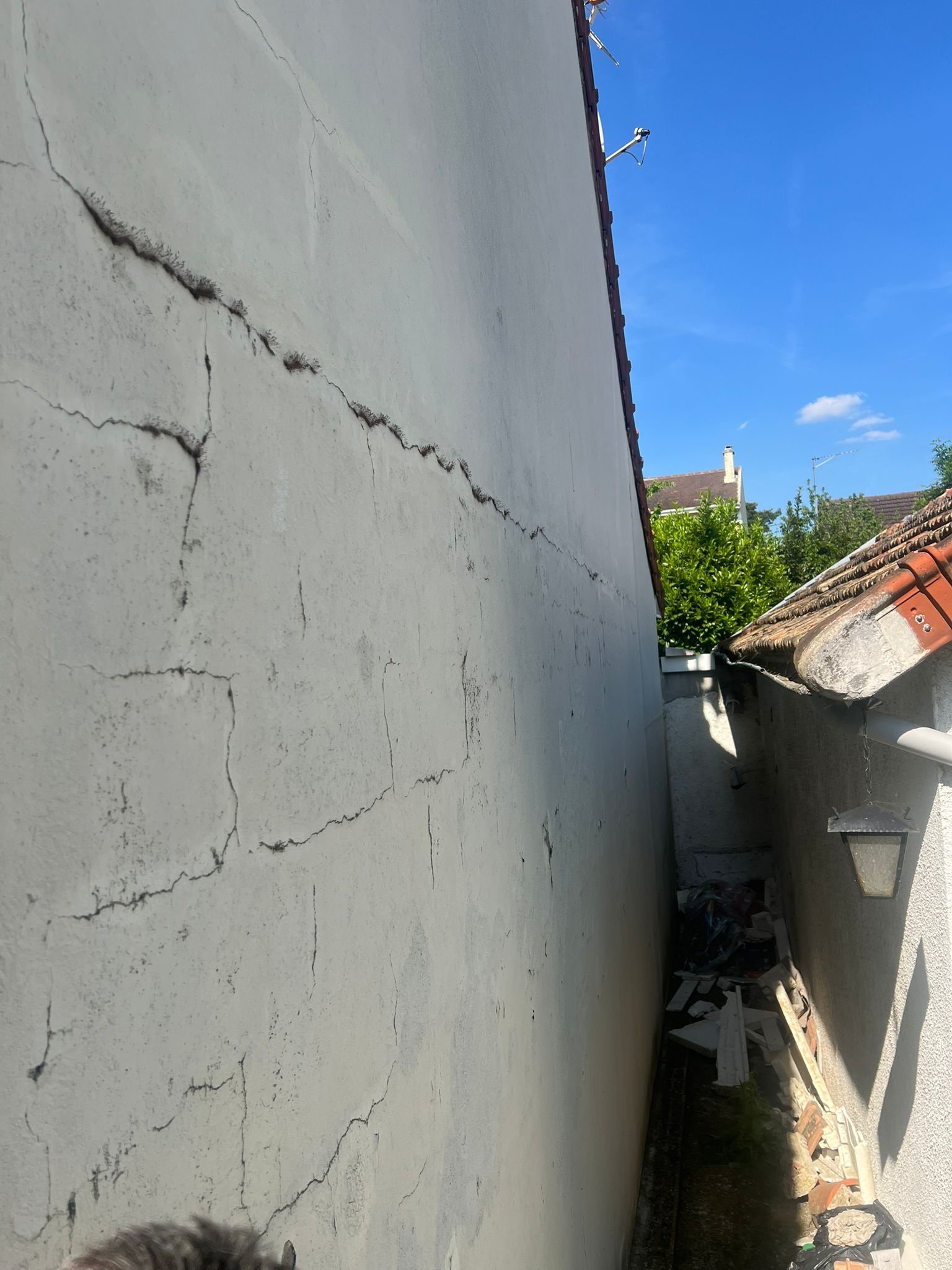 Ruelle étroite à l'extérieur, longeant un mur blanc et un toit de tuiles rouges, sous un ciel d'un bleu éclatant.