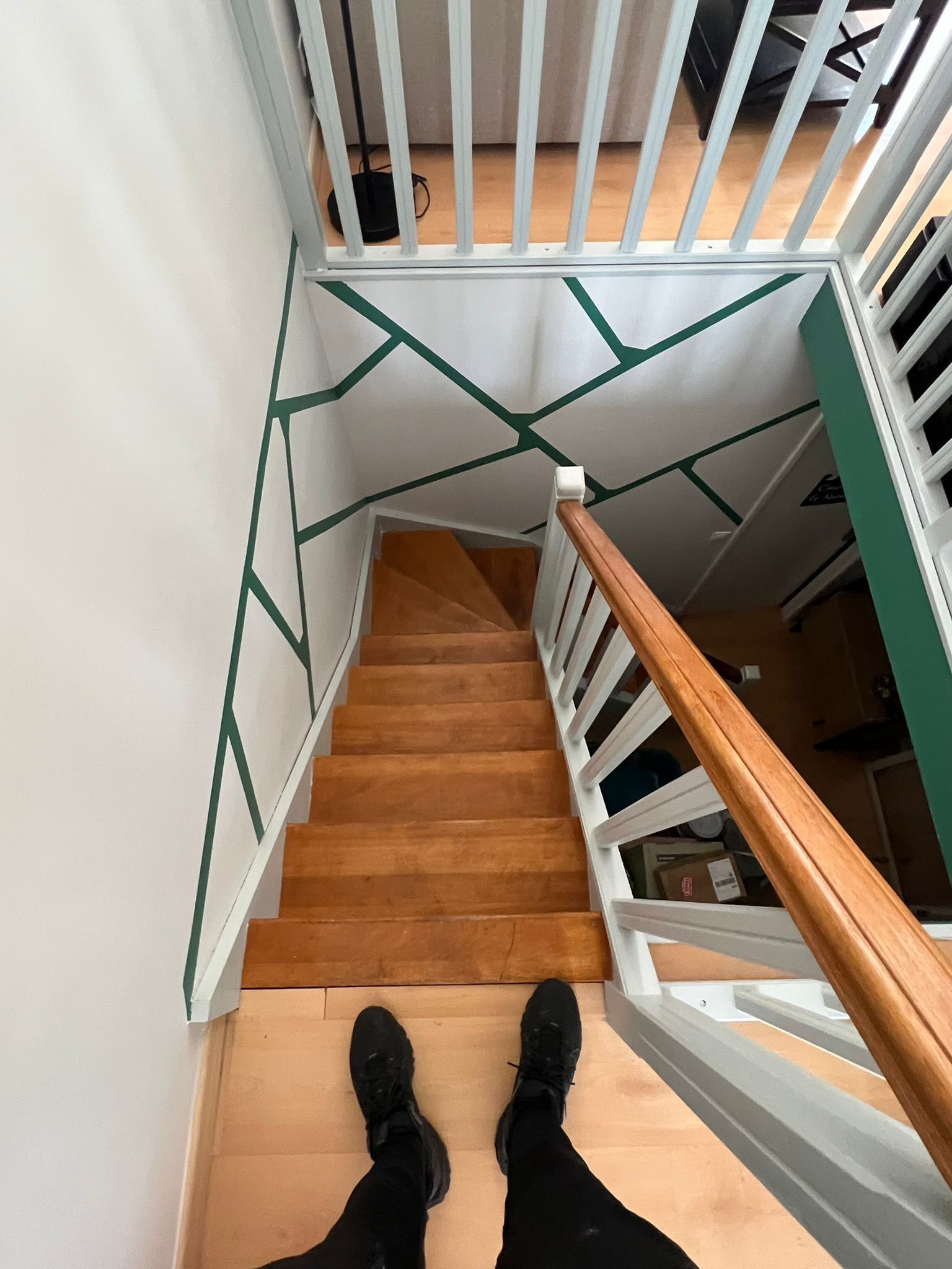 Vue de dessus d'un escalier étroit en bois aux murs blancs et aux lignes de ruban adhésif vert, vue depuis le palier supérieur.