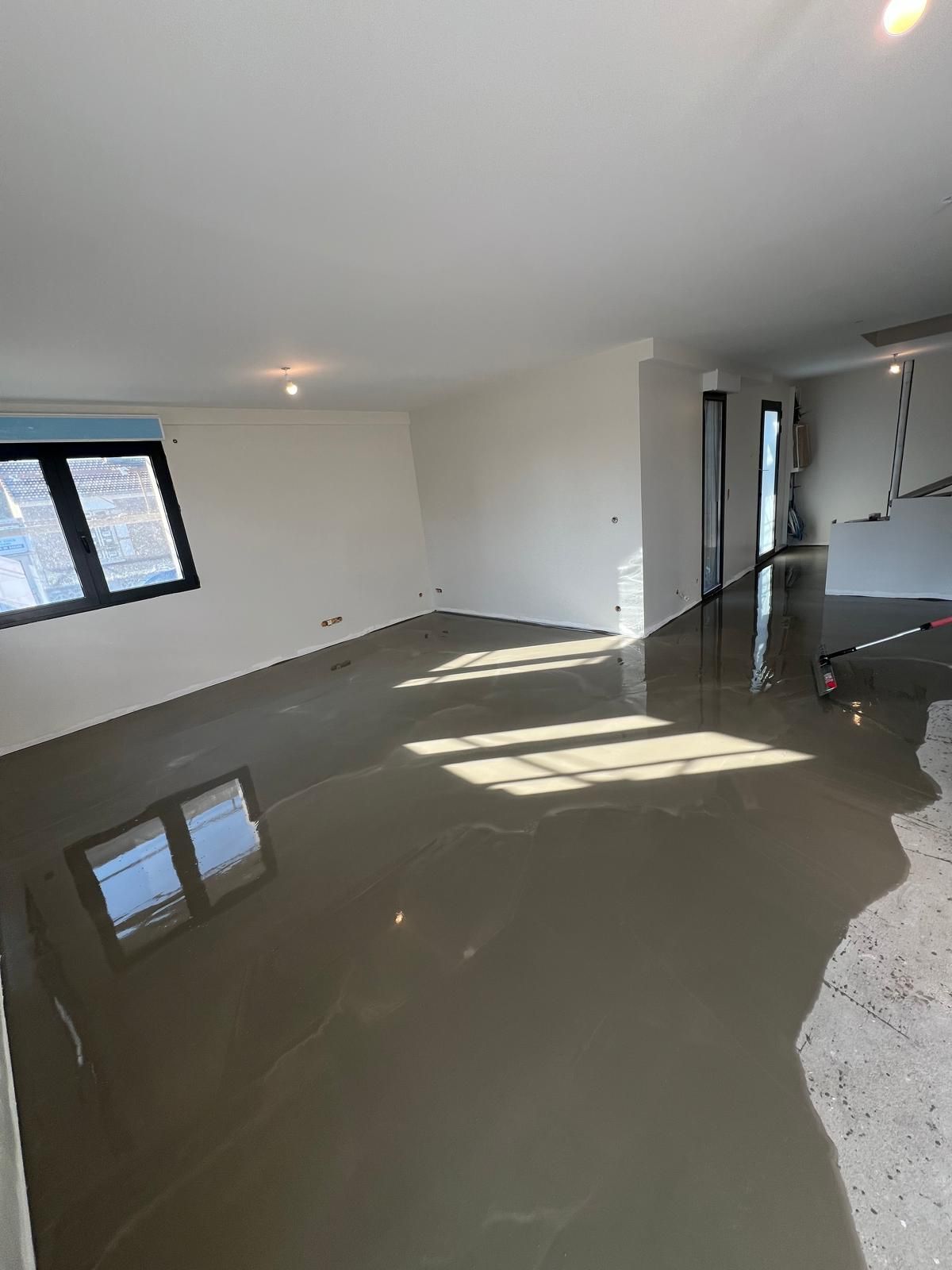 Pièce vide inondée, l'eau grise se reflétant sur les fenêtres et les plafonniers.