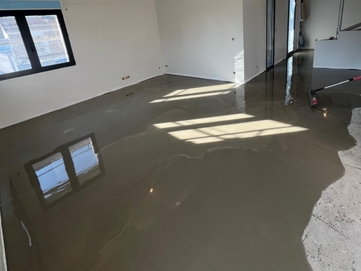 Pièce partiellement inondée, l'eau stagnante reflétant les fenêtres et la lumière sur le sol.