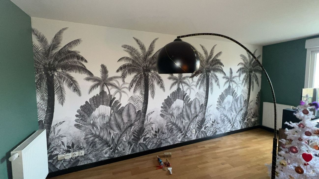 Une fresque murale représentant des palmiers orne un mur à côté d'un grand lampadaire noir en forme d'arc, dans une pièce au parquet.