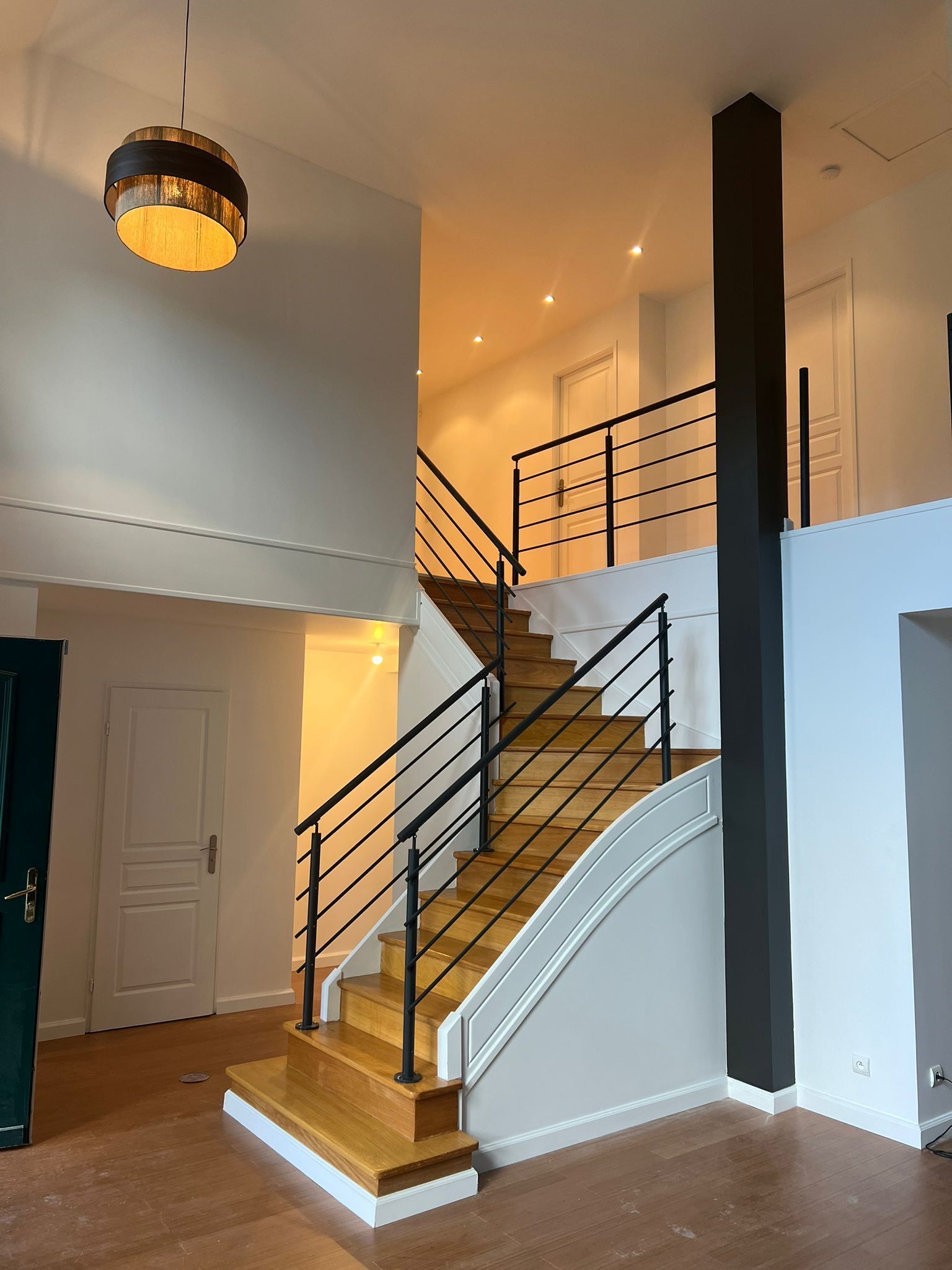 Escalier moderne avec marches en bois, rampe noire, murs blancs et un espace intérieur de style loft