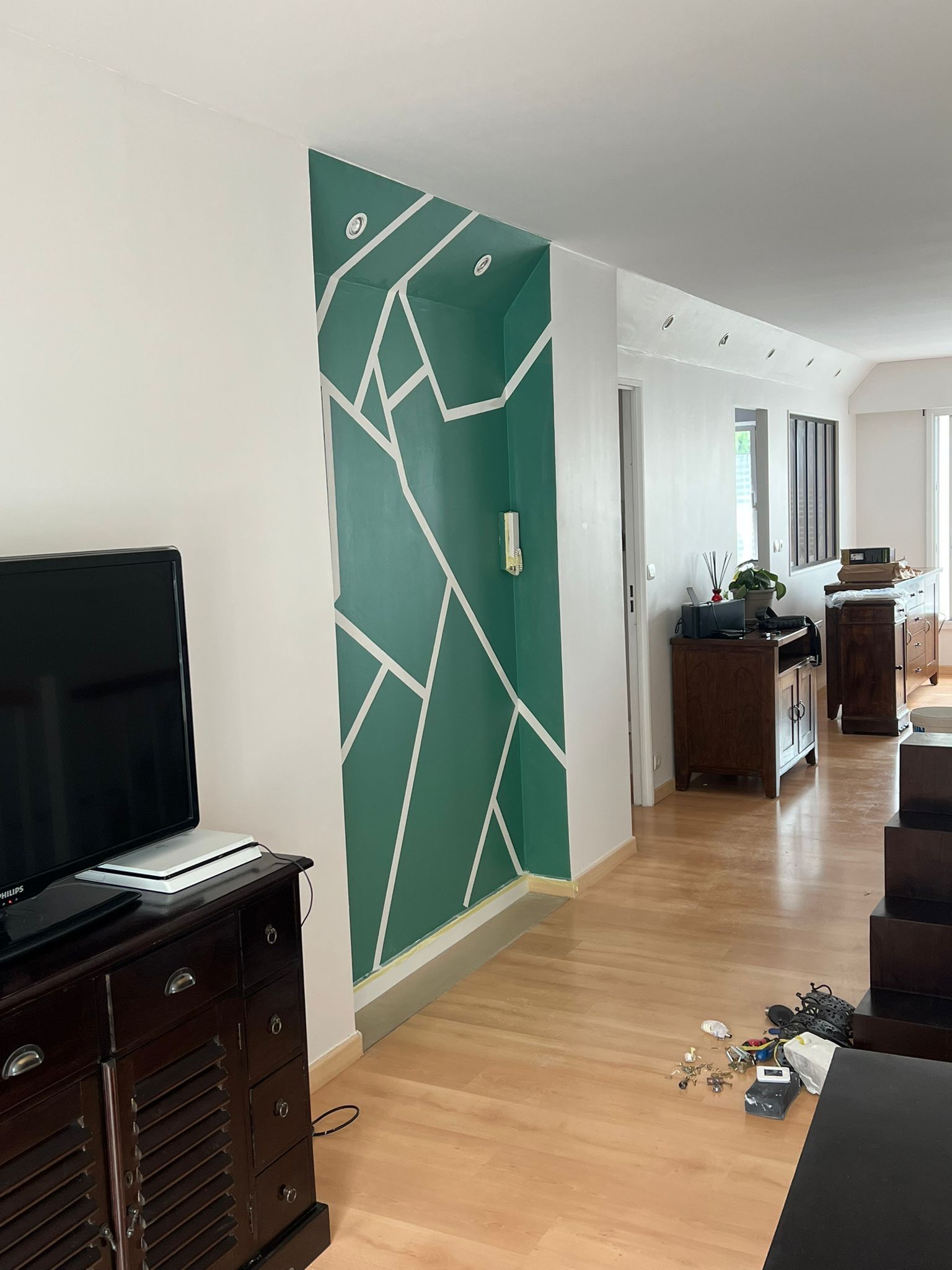 Couloir avec un mur d'accent géométrique turquoise, parquet, meuble TV et porte donnant sur une pièce lumineuse