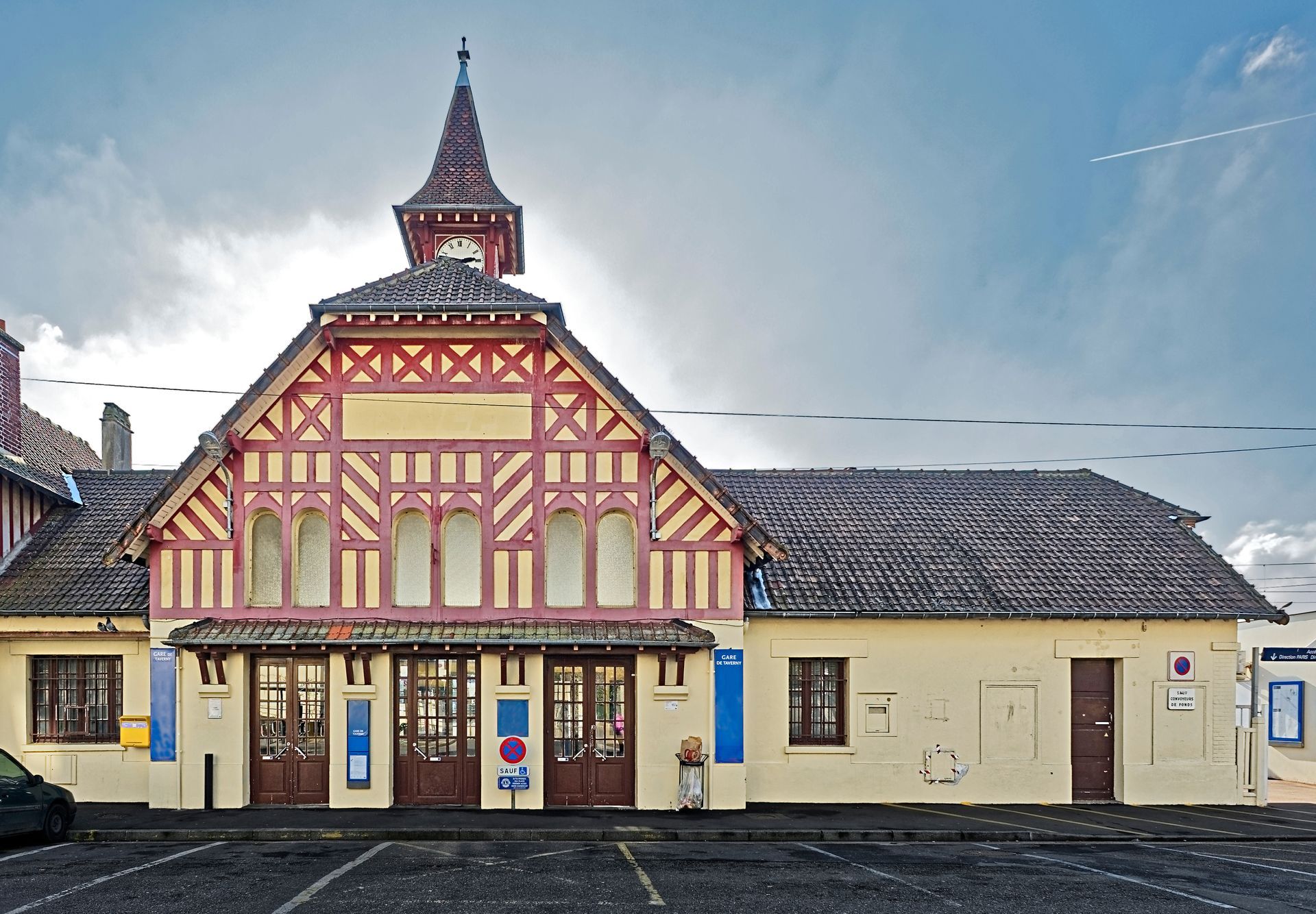 Bâtiment historique avec une façade ornée en bois rouge et une tour centrale sous un ciel nuageux