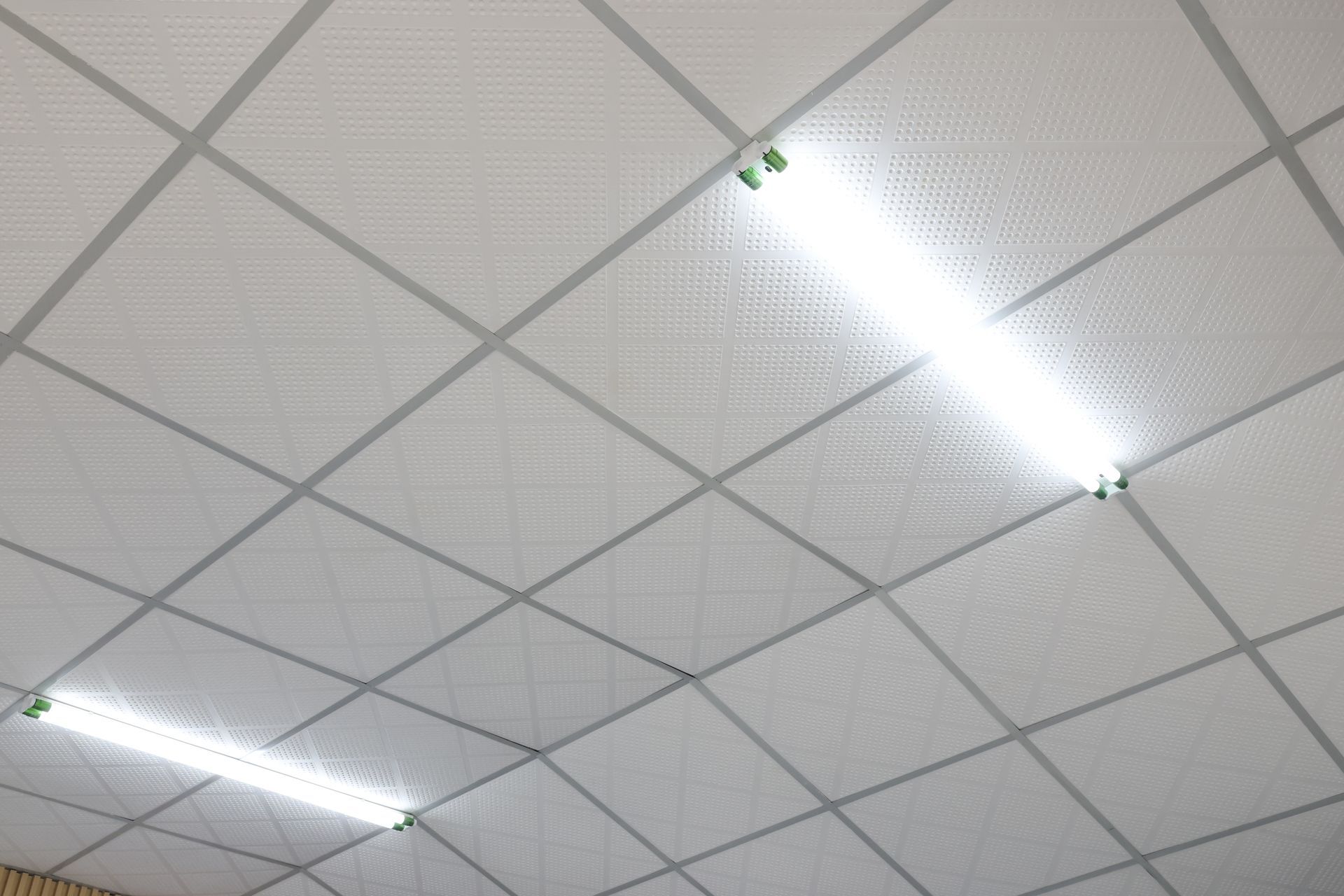 Plafond recouvert de dalles acoustiques blanches et de luminaires fluorescents à forte luminosité.