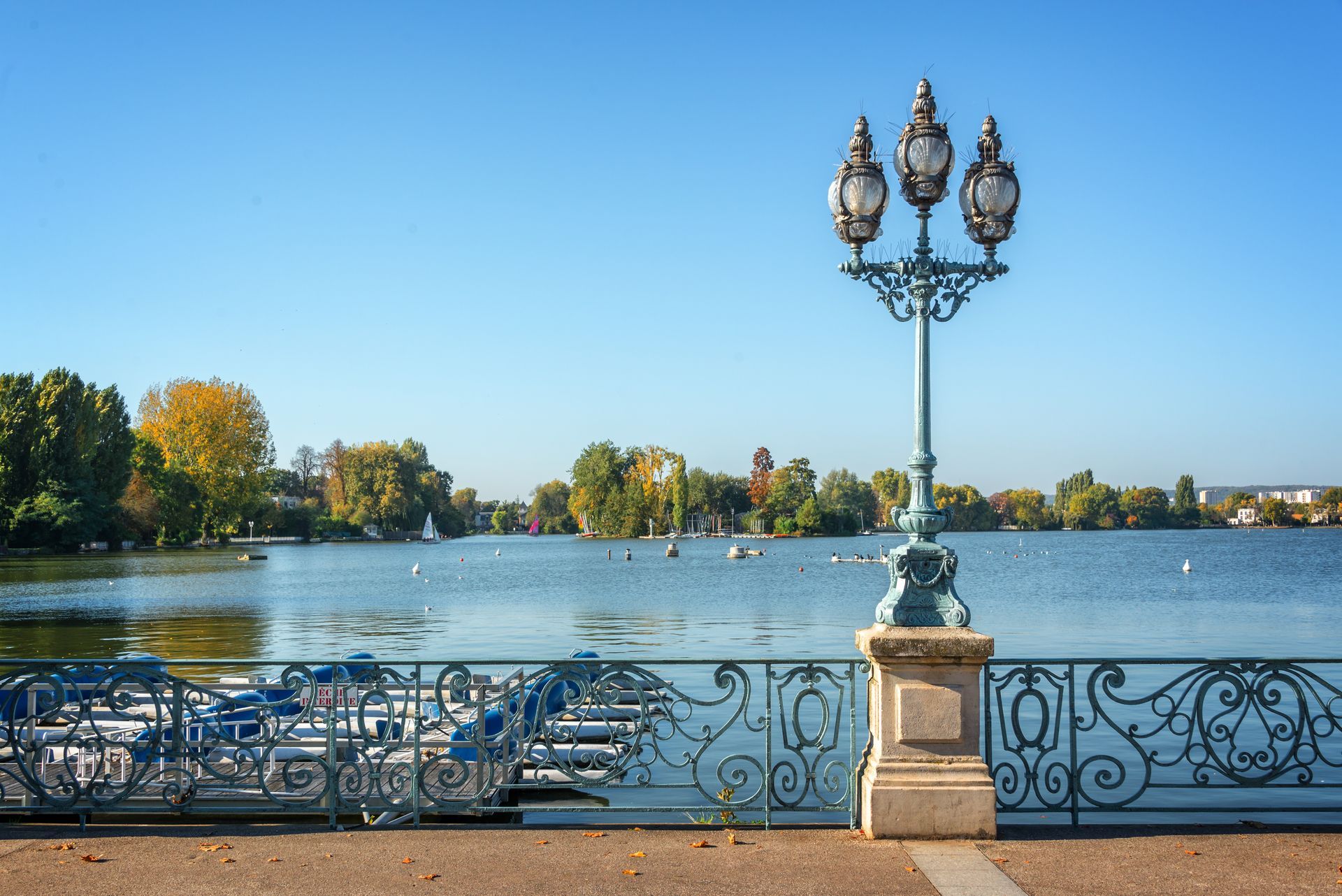 Promenade au bord du lac avec lampadaire orné, bancs et eau calme sous un ciel bleu clair