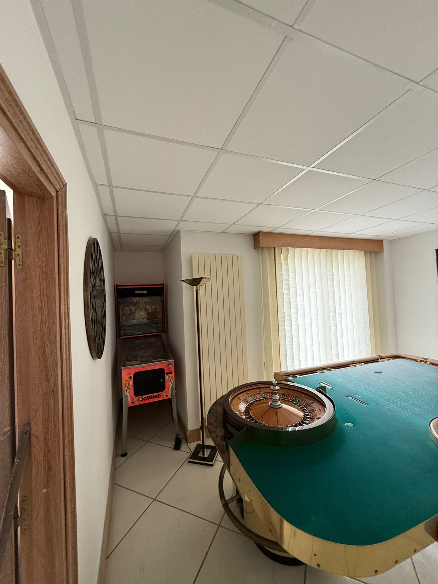 Petite salle de jeux avec une table de billard verte, un fauteuil en osier, une borne d'arcade et des rideaux aux couleurs vives.