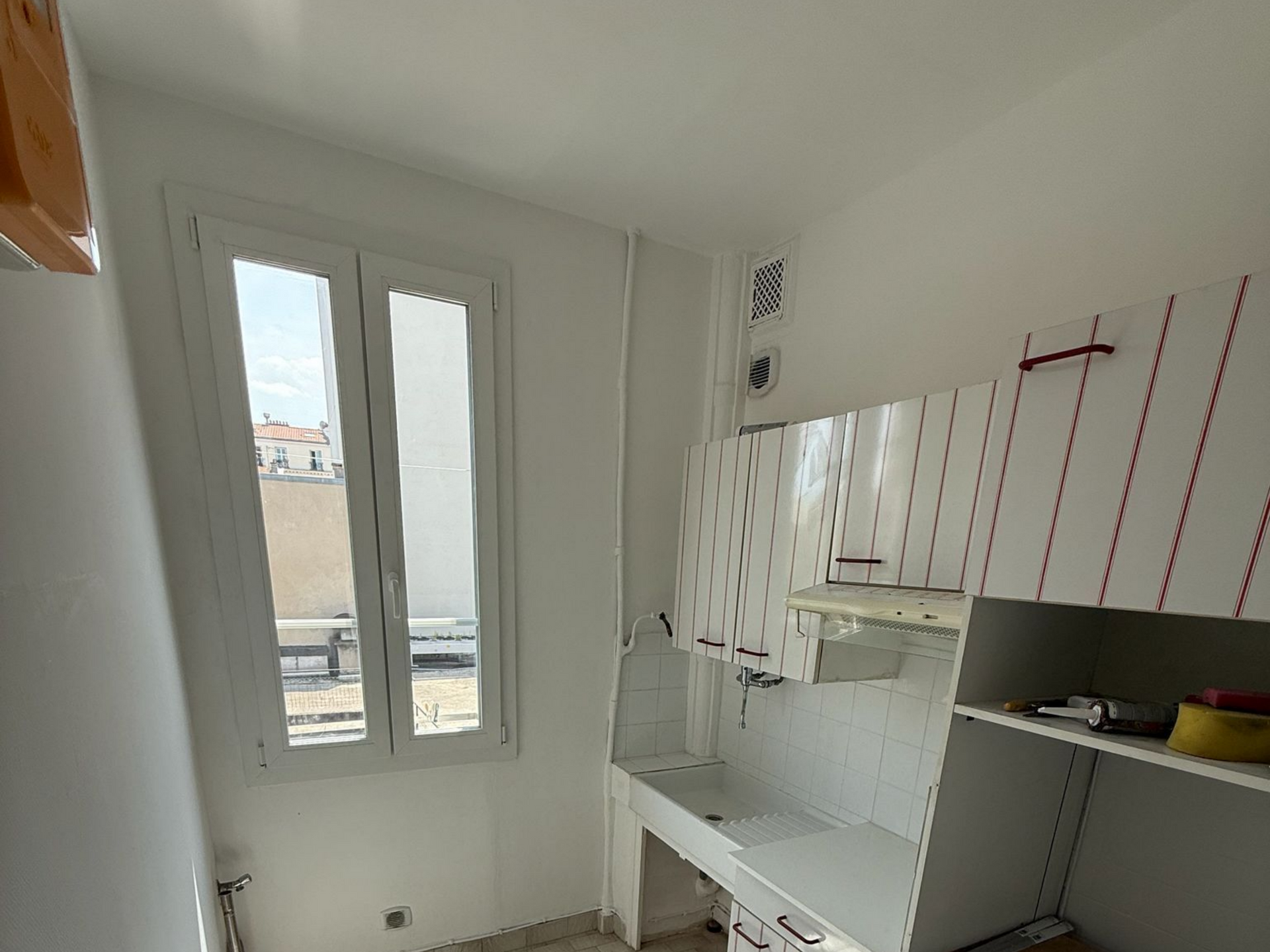 Cuisine blanche lumineuse en cours de rénovation avec placards, plan de travail, évier et fenêtre