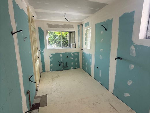 Petite pièce inachevée en cours de rénovation, avec des cloisons sèches bleues, un plafond blanc et une fenêtre au fond.