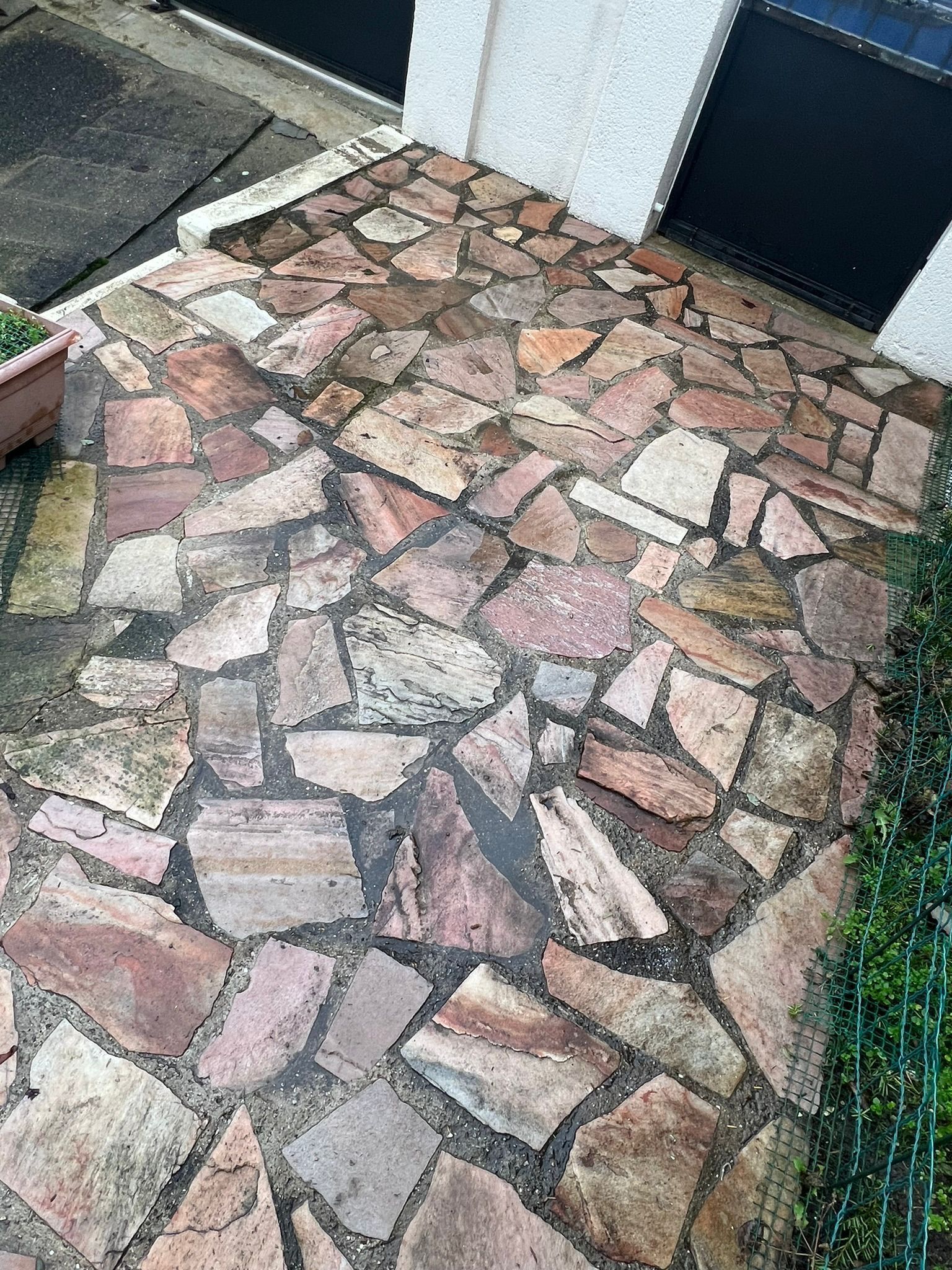 Allée pavée de pierres irrégulières roses et grises longeant une porte