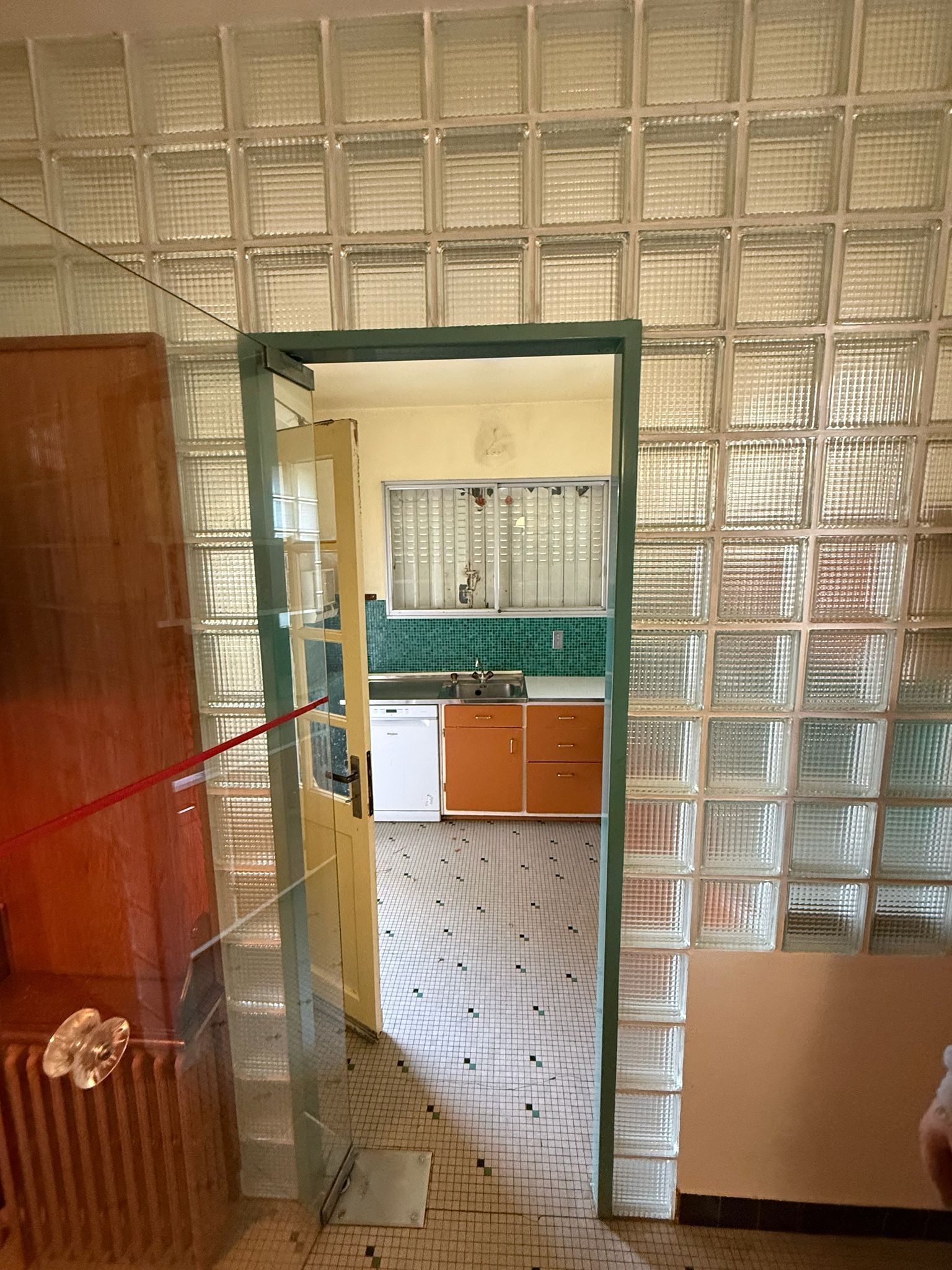 Porte donnant sur la cuisine avec murs en pavés de verre, moulures turquoise et sol en carrelage blanc à motifs.