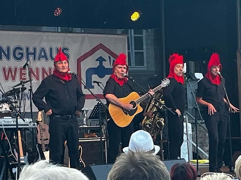 Eine Gruppe Männer steht auf einer Bühne, spielt Gitarre und singt in Mikrofone.