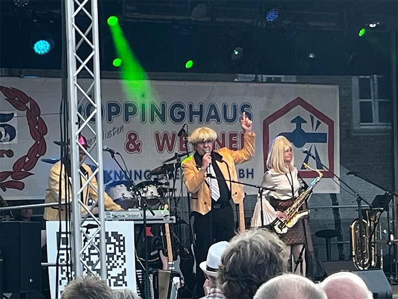 Eine Gruppe von Leuten steht auf einer Bühne, spielt Instrumente und singt in Mikrofone.