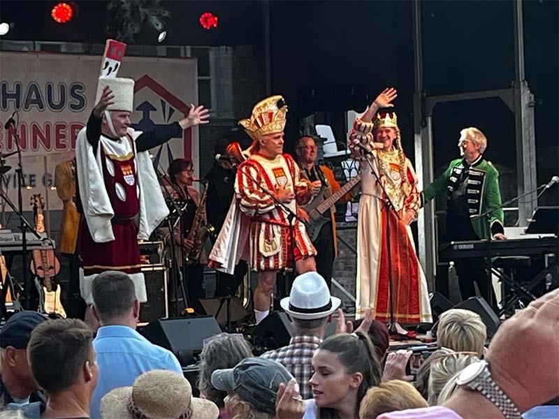 Eine Gruppe kostümierter Menschen steht vor einer Menschenmenge auf einer Bühne.