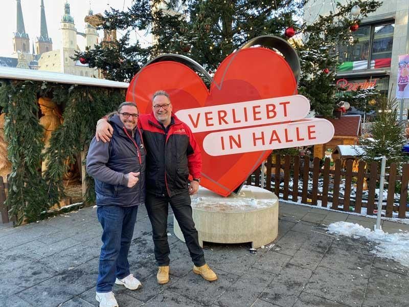 Zwei Männer stehen vor einem großen roten Herz mit der Aufschrift „Verliebt in Halle“