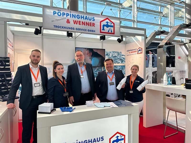 Eine Gruppe von Menschen steht auf einer Messe vor einem Stand.