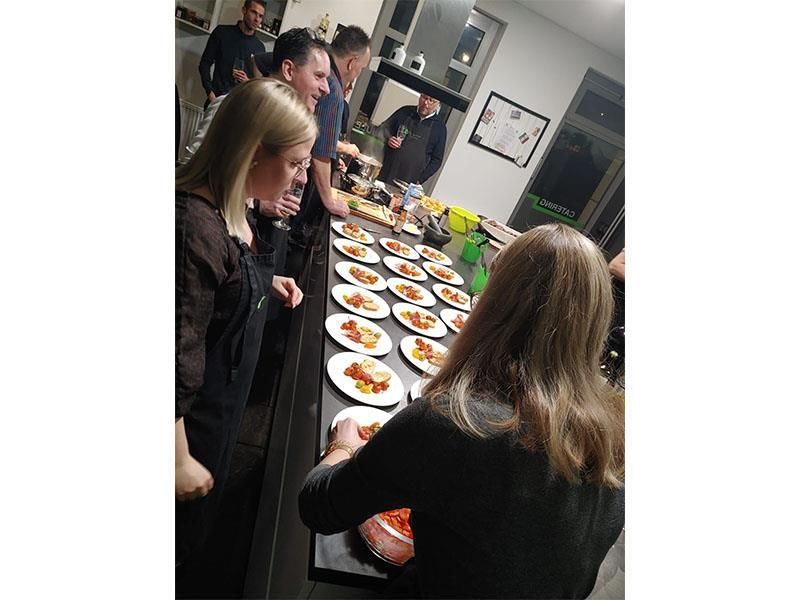 Eine Gruppe von Leuten steht um einen Tisch herum, auf dem Teller mit Essen stehen.
