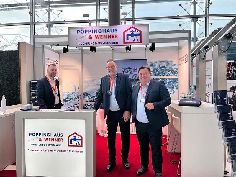 Drei Männer stehen vor einem Stand von Poppinghaus & Wenner.