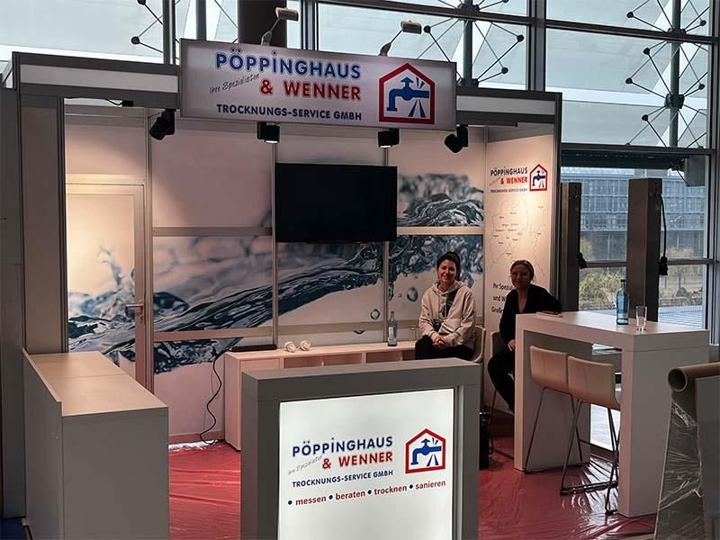 Zwei Personen sitzen an einem Tisch vor einem Poppinghaus-Schild