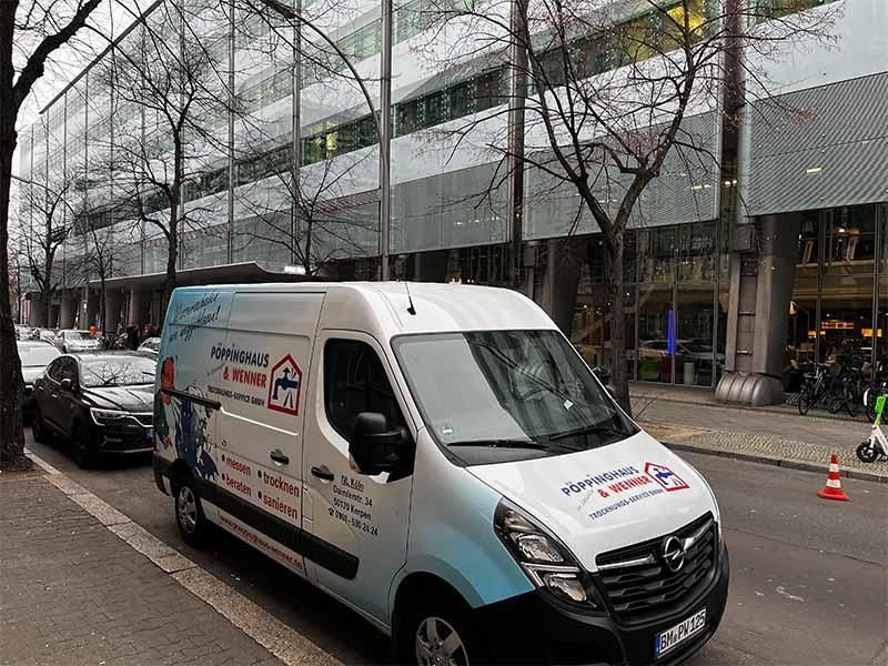 Ein weißer Lieferwagen steht am Straßenrand vor einem Gebäude.