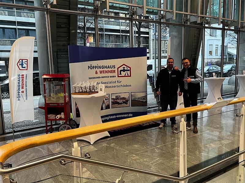 Zwei Männer stehen nebeneinander vor einem Display in einer Lobby.