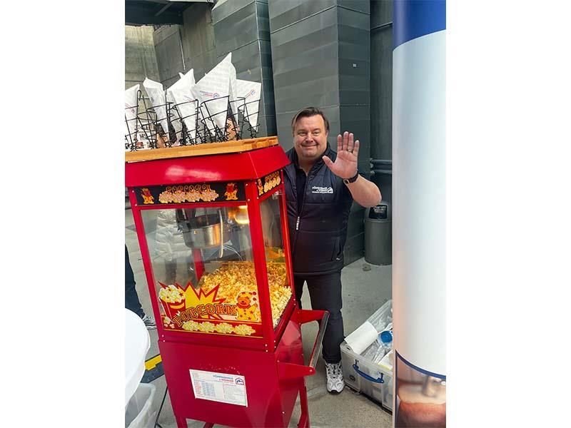 Ein Mann steht neben einer roten Popcornmaschine.