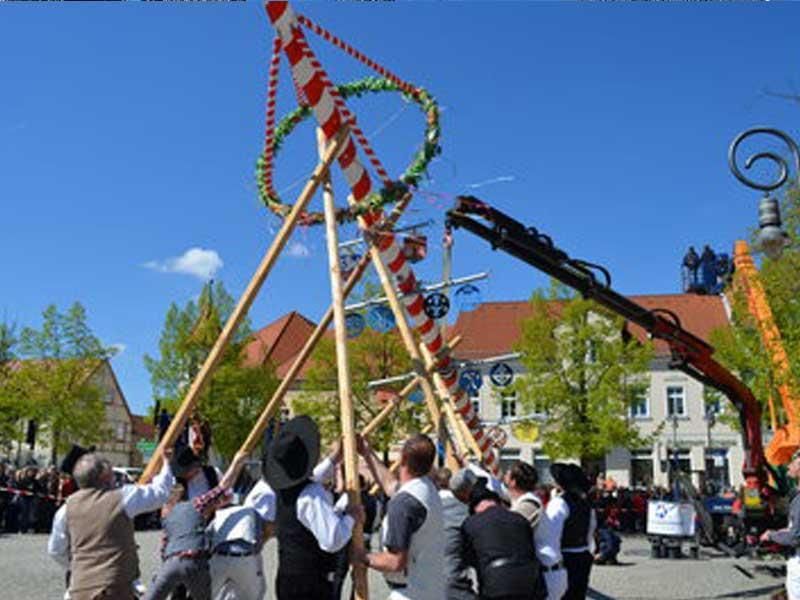 Eine Gruppe von Menschen steht um einen Mast herum, im Hintergrund ist ein Kran zu sehen.