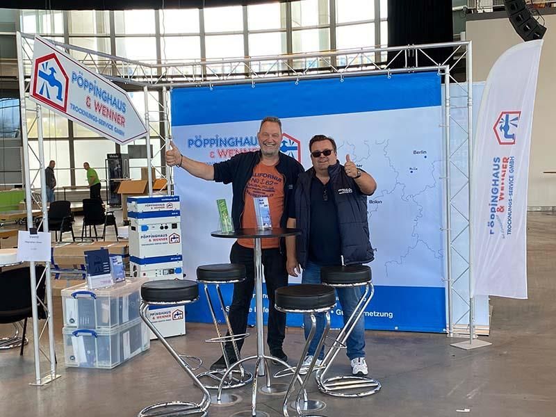 Zwei Männer posieren für ein Foto vor einem Schild mit der Aufschrift 