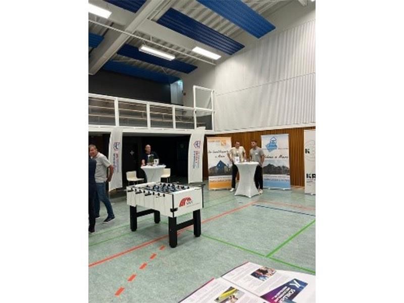 Eine Gruppe von Leuten steht in einer Turnhalle um einen Tischfußballtisch herum.