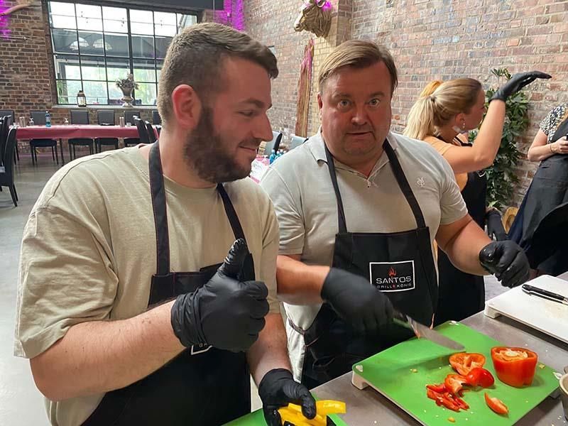 Zwei Männer schneiden Paprika auf einem grünen Schneidebrett.