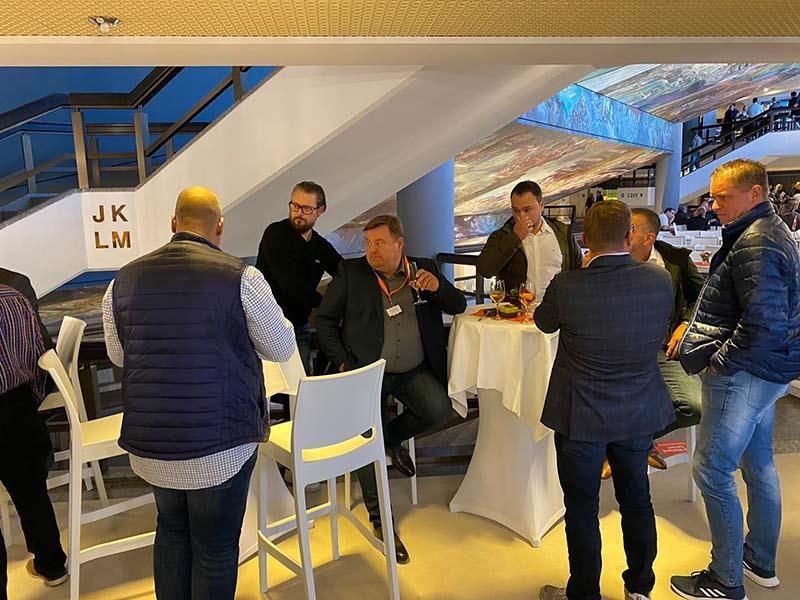 Eine Gruppe von Männern steht um Tische in einem Raum mit einem Schild mit der Aufschrift „jk lm“