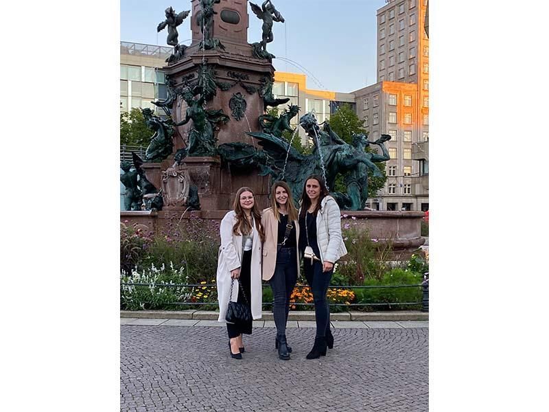 Drei Frauen posieren vor einer Statue für ein Foto.