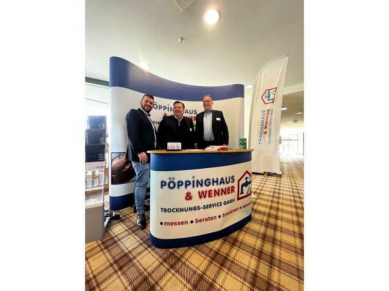 Drei Männer stehen hinter einem Tresen mit der Aufschrift Poppinghaus & Wenner