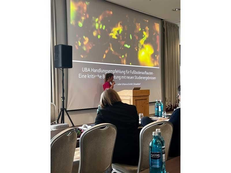 Eine Frau hält in einem Konferenzraum vor einem großen Bildschirm eine Präsentation.