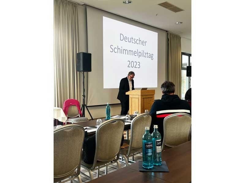 Ein Mann steht an einem Podium vor einem Bildschirm mit der Aufschrift „Deutsche Schimmelpilze 2021“