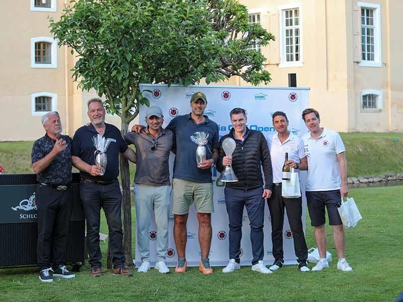 Eine Gruppe von Männern steht mit Trophäen in den Händen nebeneinander auf einem Golfplatz.