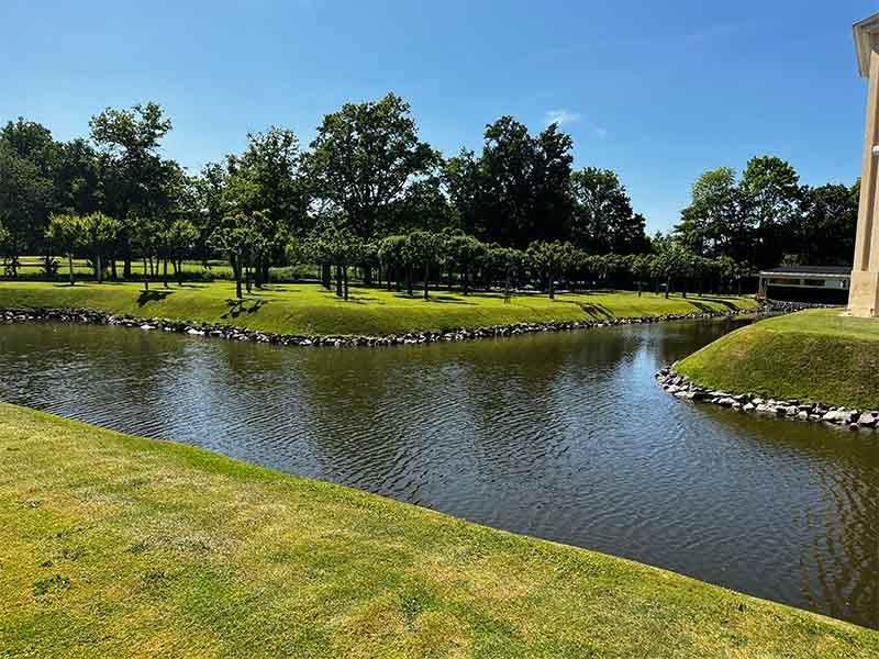 Ein großes Gewässer, umgeben von Gras und Bäumen