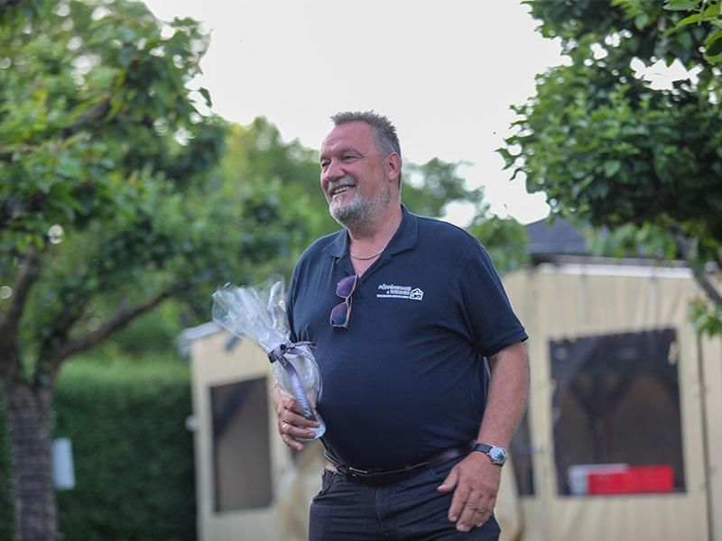 Ein Mann mit Bart hält einen Blumenstrauß vor einem Zelt.