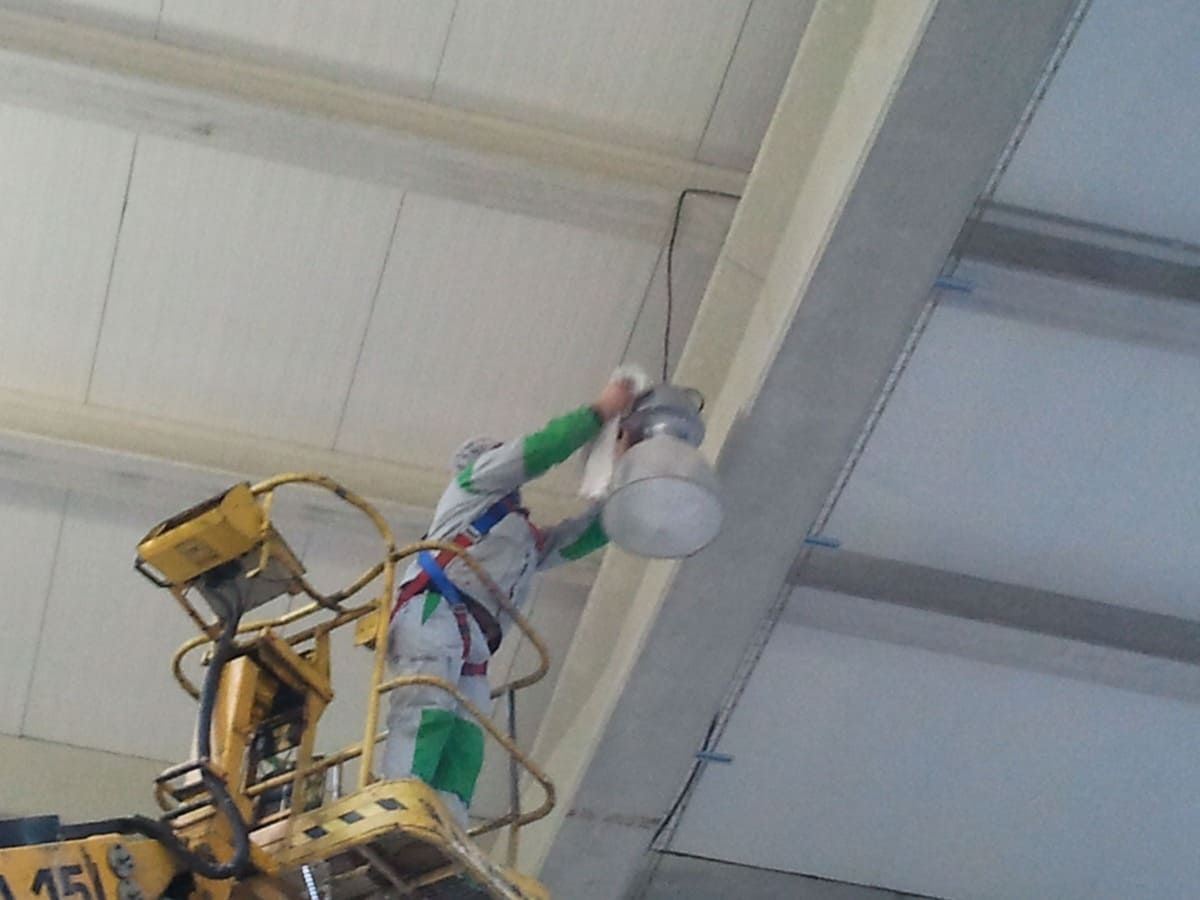 Una cesta elevadora amarilla trabajando cerca de una viga del techo en un almacén industrial.