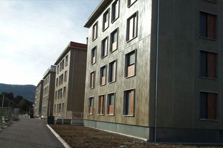 Edificios de apartamentos modernos junto a una carretera asfaltada, con montañas al fondo.